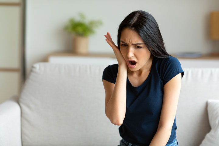 Girl Suffering From Tooth Pain Touching Cheek Sitting At Home before visiting North Hills Implant & Oral Surgery in Raleigh, NC 27609-6518